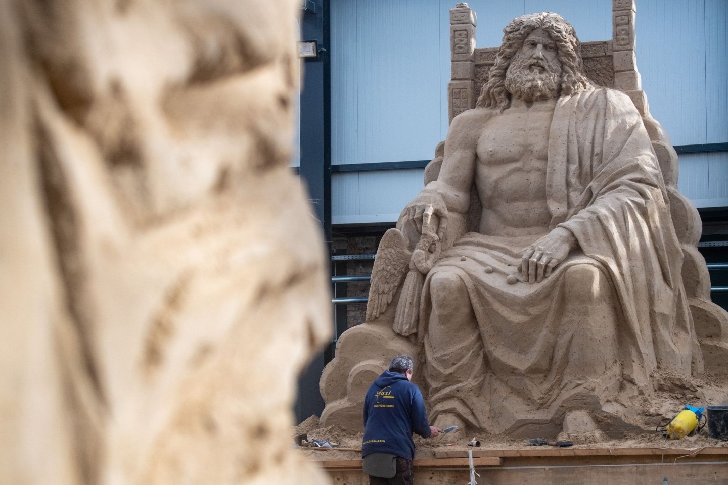 Ein Mann arbeitet an einer Sandskulptur des Göttervaters Zeus auf seinem Thron.