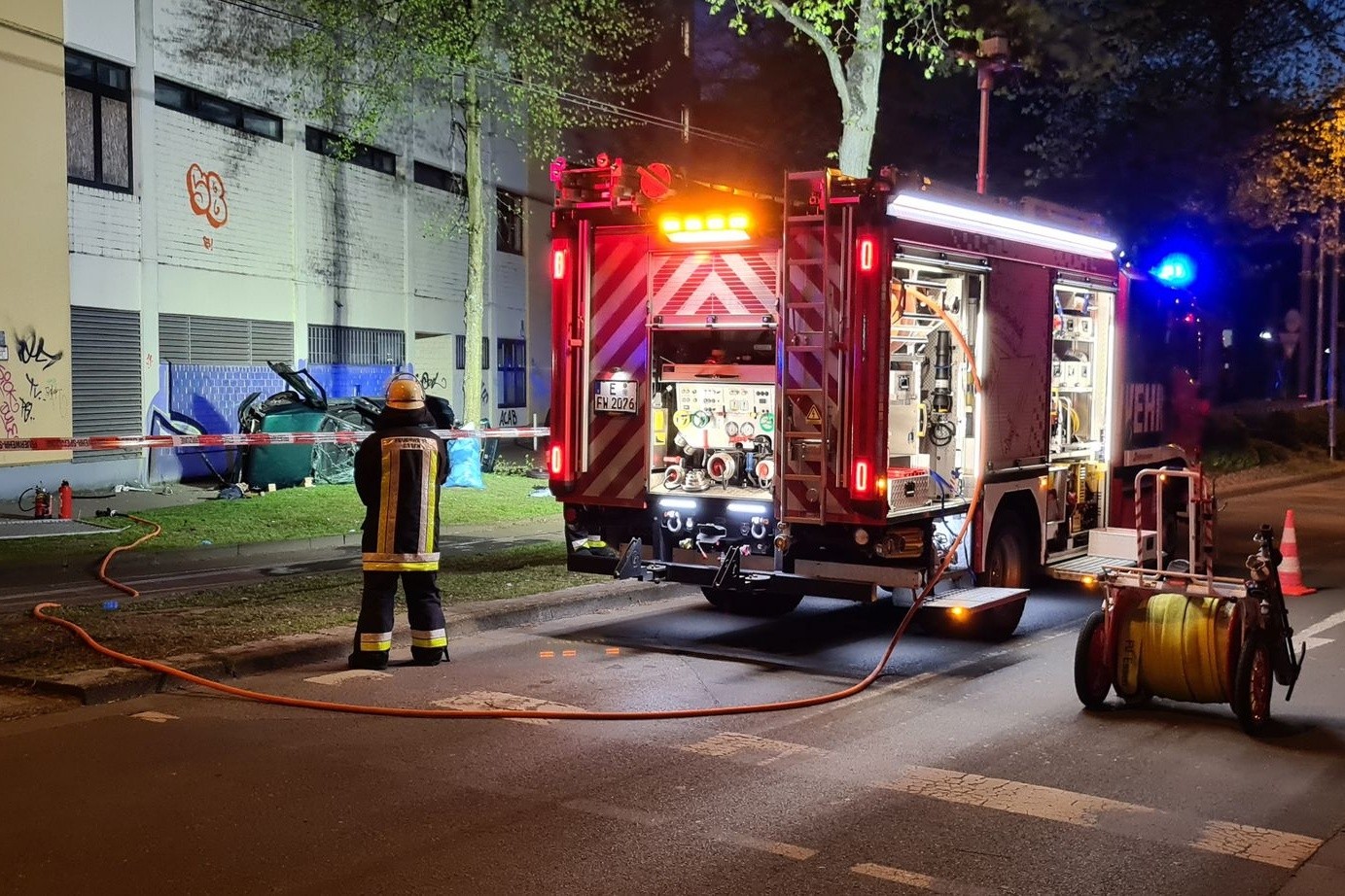 Ein Feuerwehrmann steht neben dem Wrack eines Autos, in dem zwei junge Männer aus der obersten Etage eines Parkhauses gestürzt und ums Leben gekommen sind.