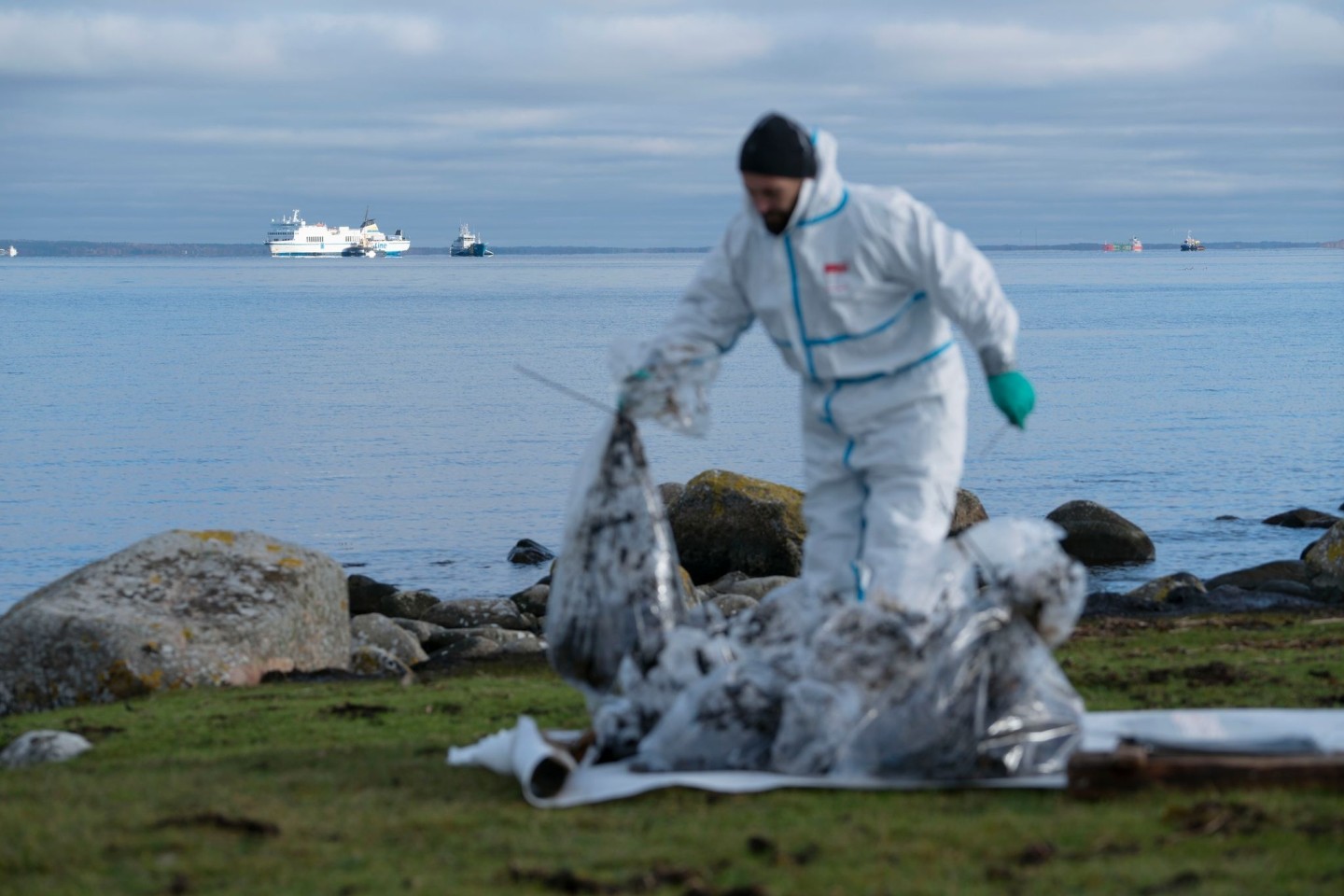 Ein Mann in Schutzkleidung arbeitet am Strand. Bei der vor der südschwedischen Küste feststeckenden Ostseefähre «Marco Polo» (hinten, l) ist erneut Öl ausgetreten.