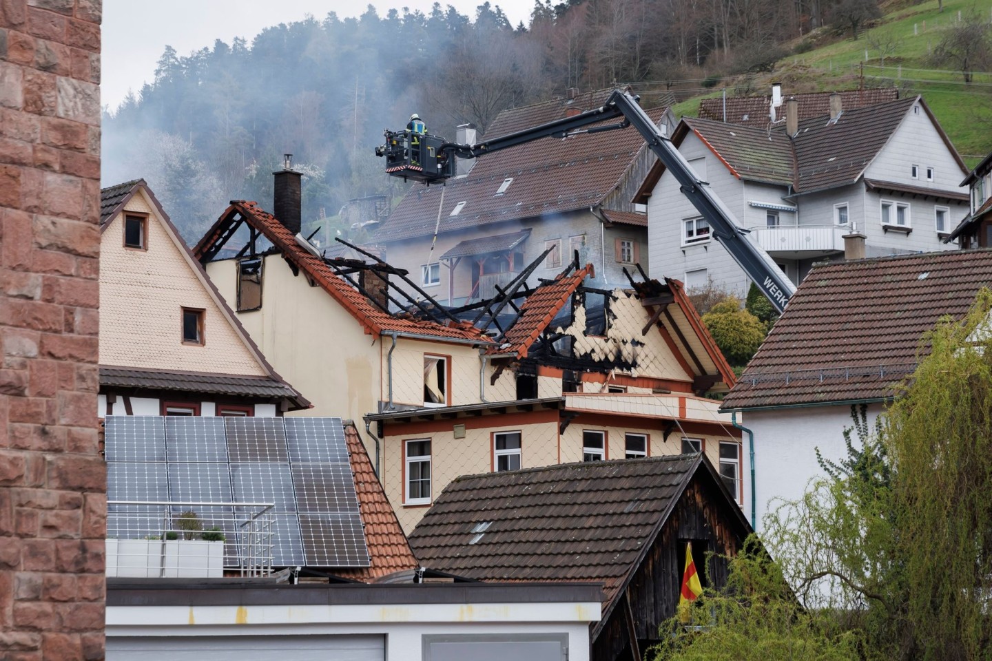 Mit einem Spezialfahrzeug werden Feuerwehrleute von oben in das abgebrannte Haus abgelassen.