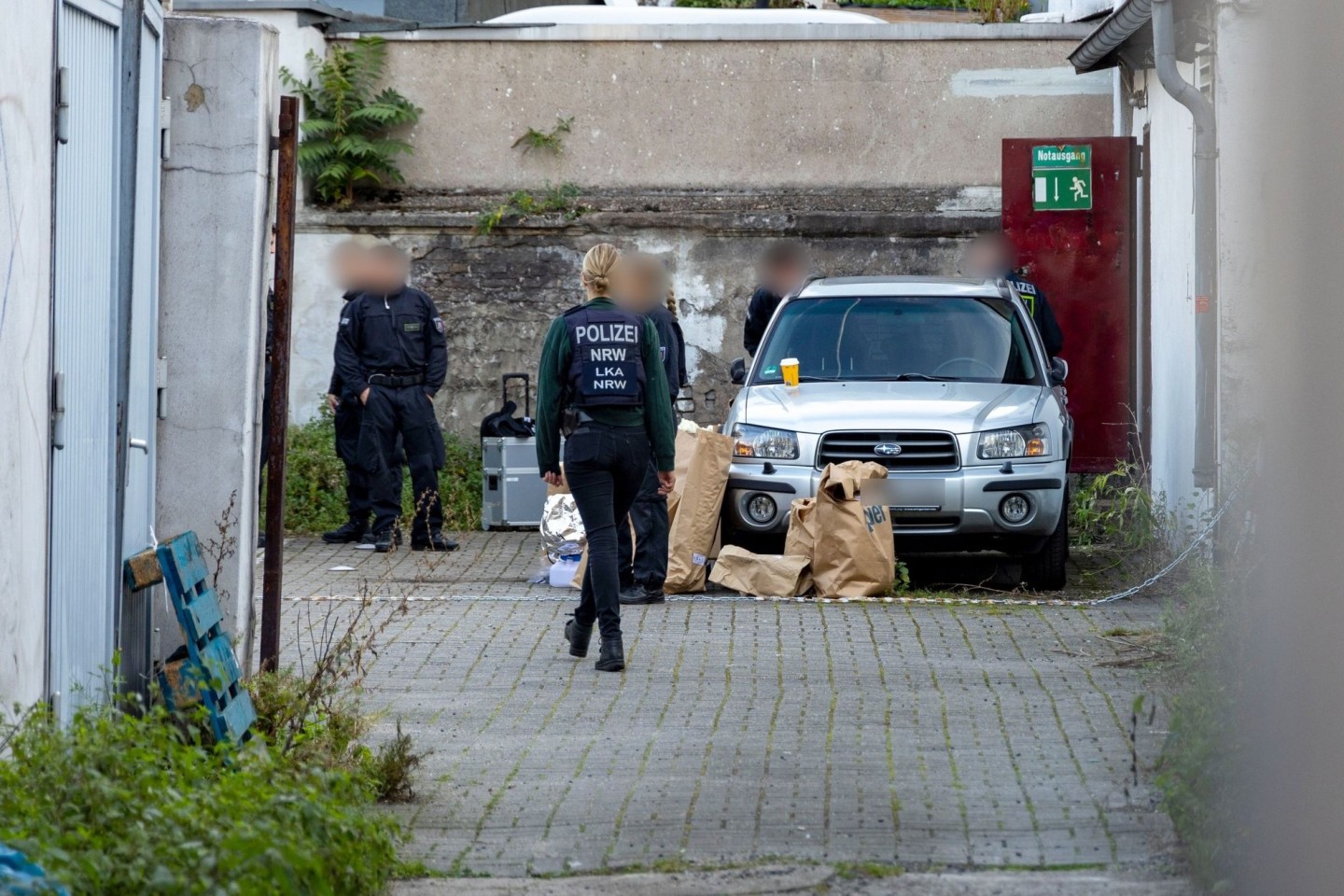 Polizistinnen und Polizisten stehen in einem Hinterhof in der Duisburger Innenstadt, auf dem Boden stehen Papiertüten mit Beweismitteln.