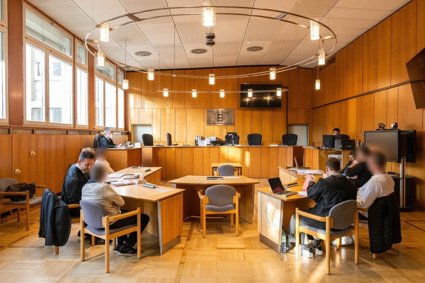 Vier Angeklagte sitzen mit ihren Verteidigern im Vorfeld der Verhandlung im Saal des Landgerichts Offenburg.