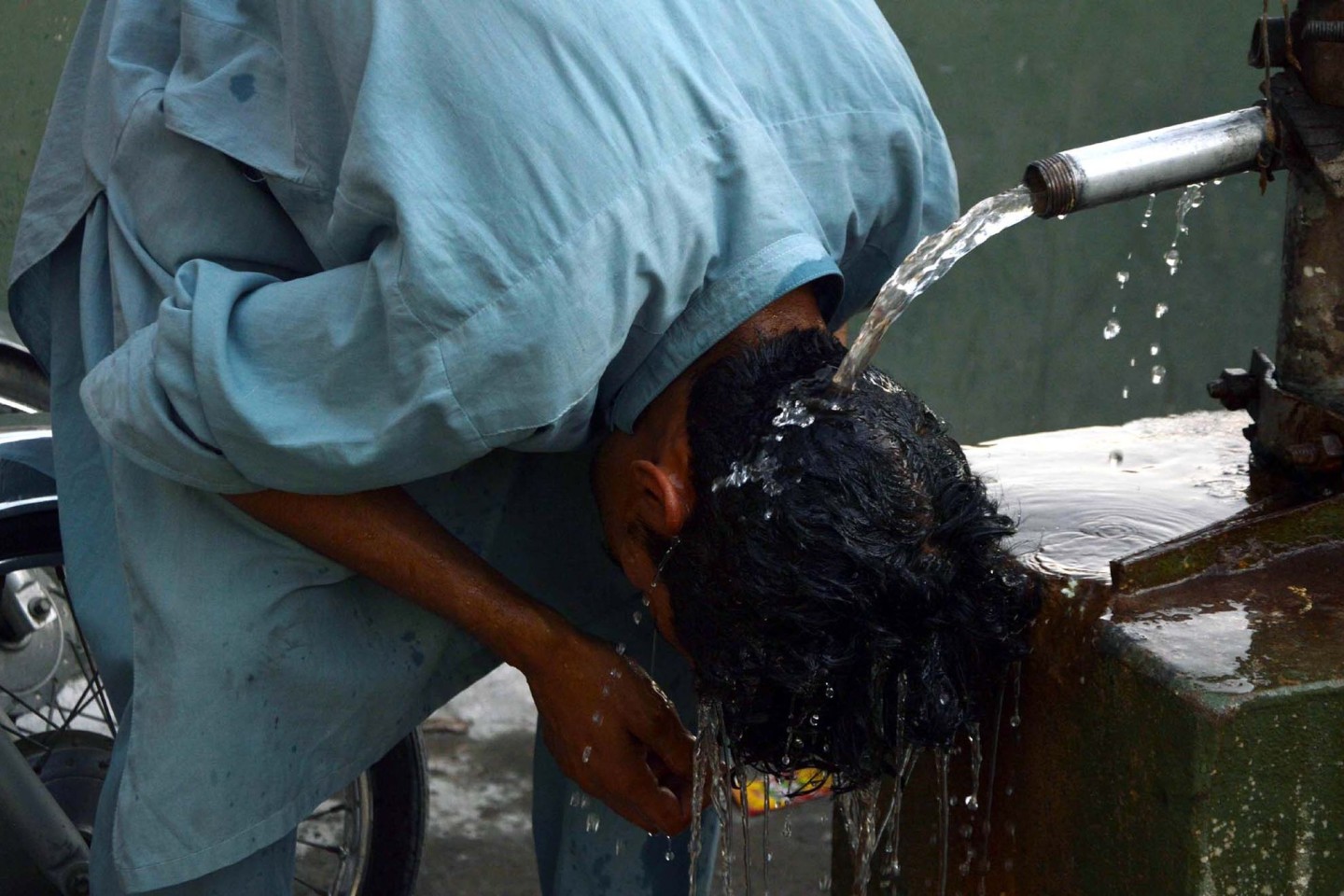 Ein junger Mann in Pakistan erfrischt seinen Kopf unter einem Wasserhahn.