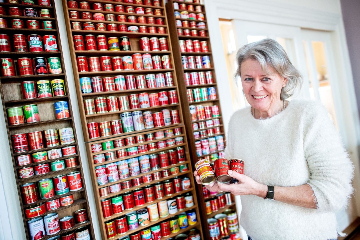 Gunda Tuchenhagen in ihrem Esszimmer vor einer Regalwand mit zahlreichen Tomatenmarkdosen aus verschiedenen Ländern.