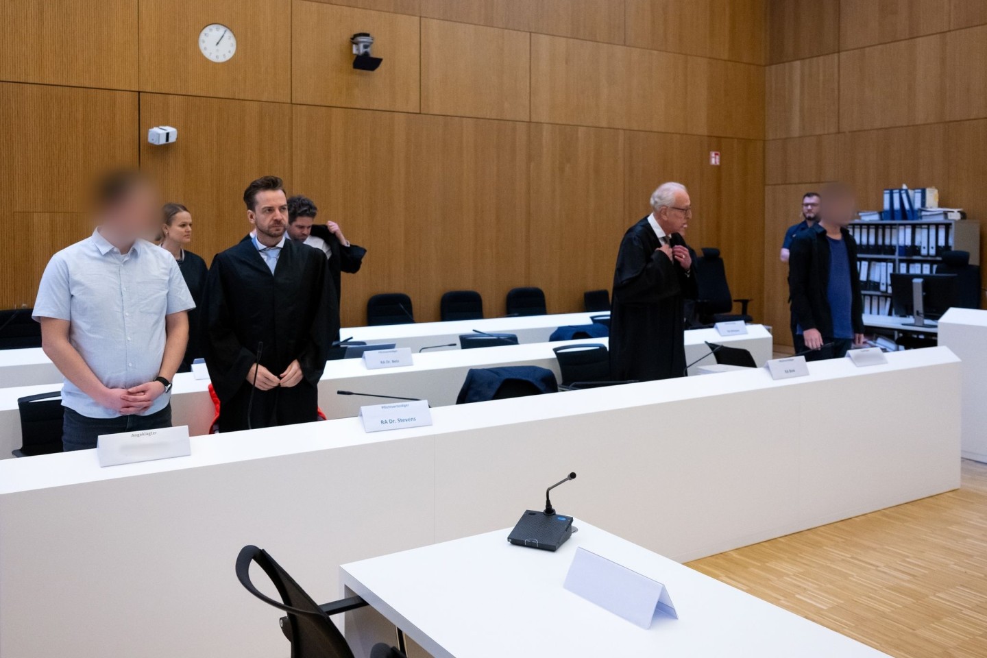 Im Hochsicherheitsgerichtssaal des Landgerichts München II stehen die zwei wegen Mordes angeklagten Männer (l und r) neben ihren Rechtsanwälten.