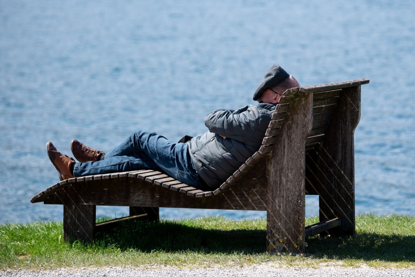 Ein Mann liegt am Ufer des Tegernsees in der Sonne und deckt sein Gesicht ab.