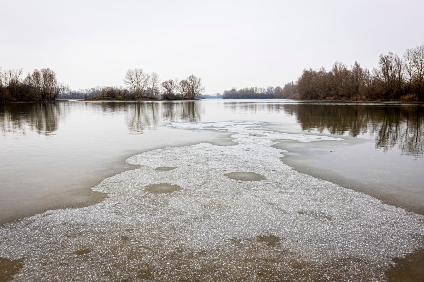 Eine dünne Eisschicht bedeckt bei trübem Wetter die Wasseroberfläche der Koldinger Seen in der Region Hannover.