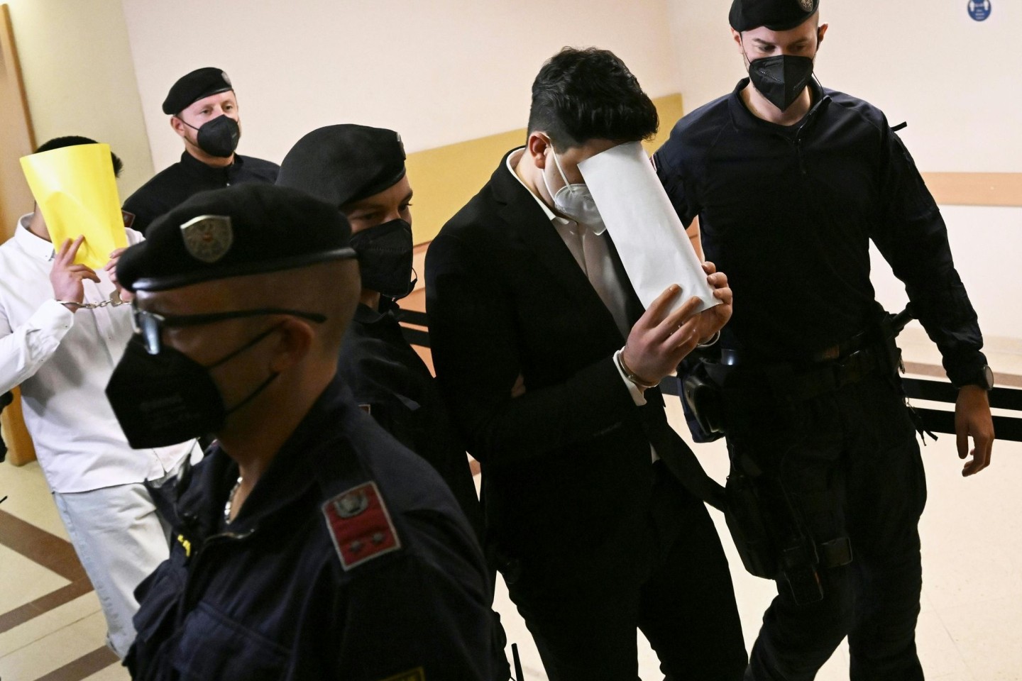 Zwei Angeklagte gehen zu Beginn des Prozesses im Wiener Landgericht in Handschellen und begleitet von Justizbeamten über einen Gang.