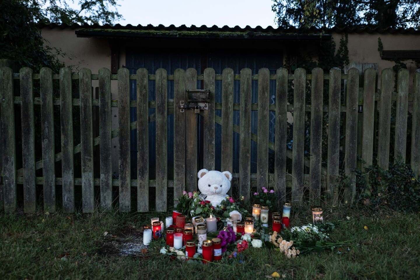Kerzen, Blumen und ein großer Plüschteddy vor einem Zaun am Fundort der Leiche einer 14-Jährigen.