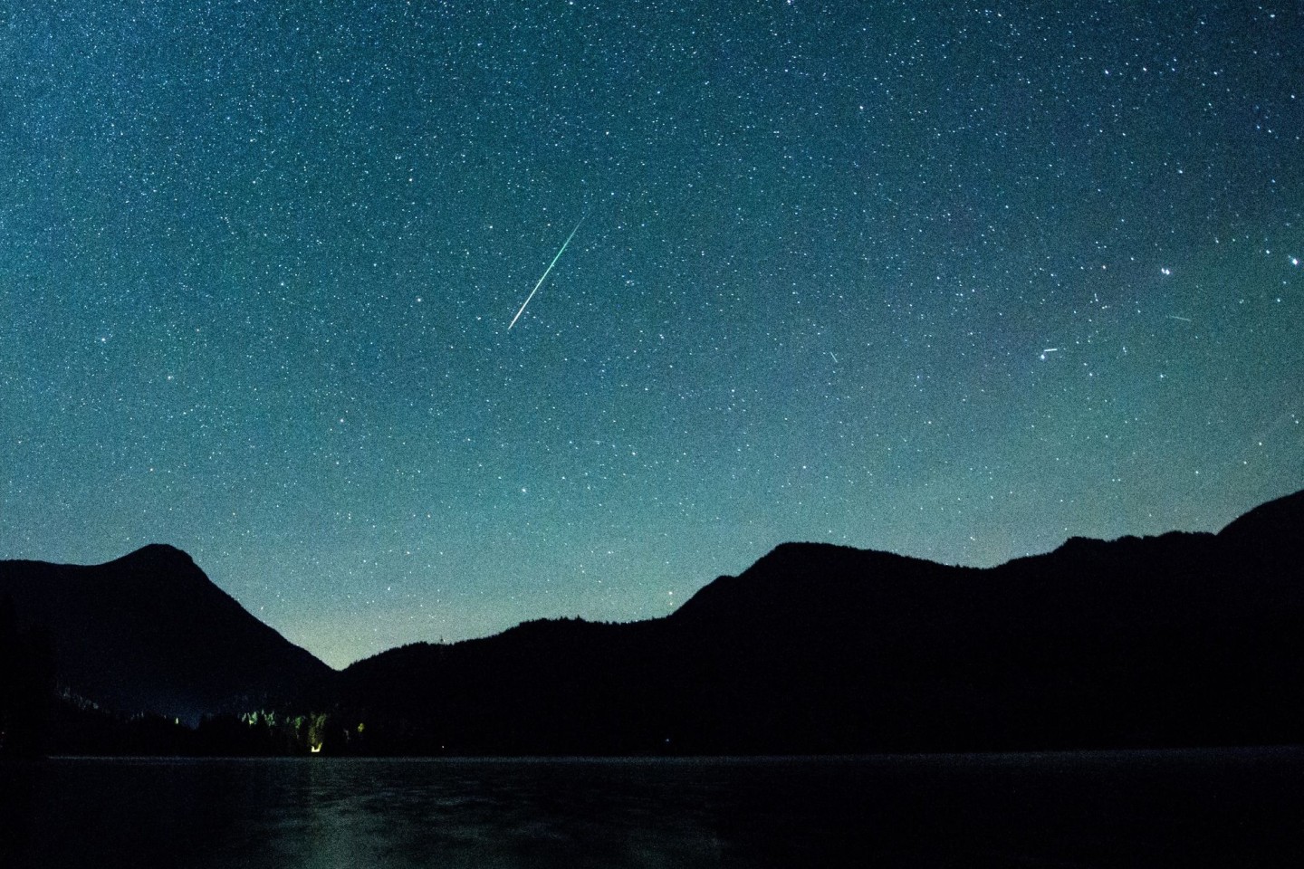 Eine Sternschnuppe leuchtet neben der Milchstraße am Himmel über dem Walchensee.
